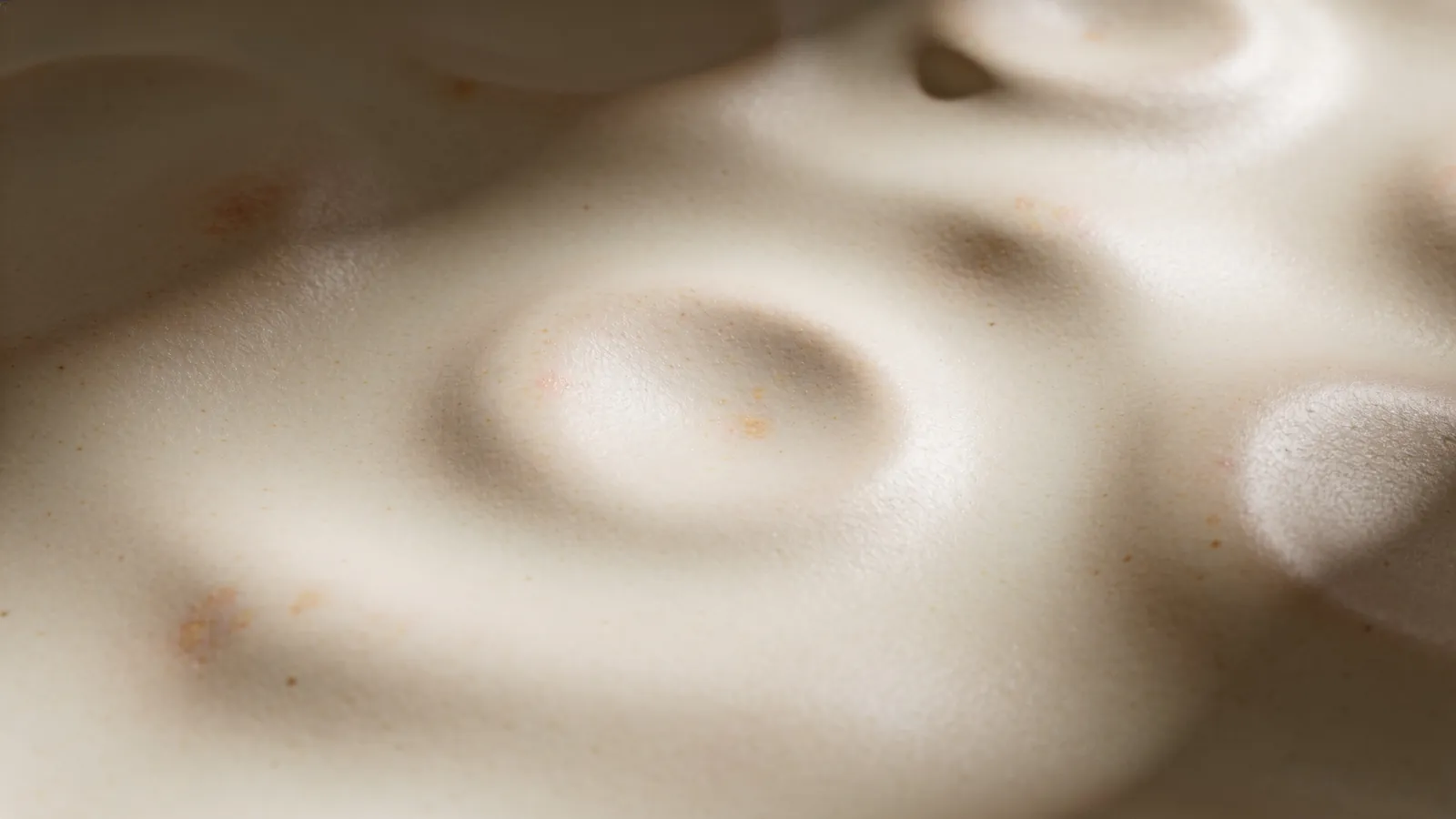Ceramic surface with shallow dimples and faint spots, an abstract picture of marks versus scars