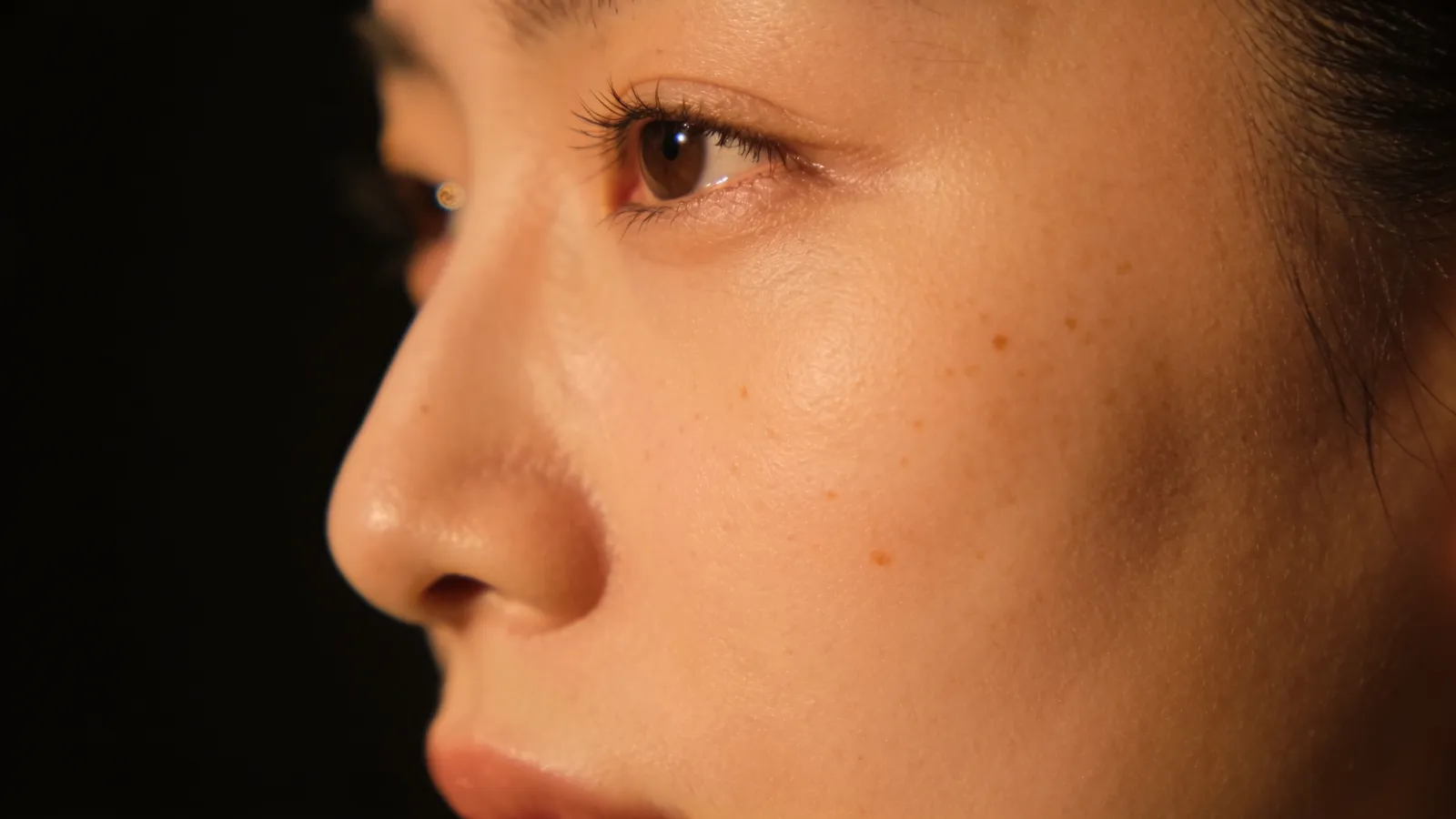 Close-up of cheek skin with a few small light-brown sun spots and freckles