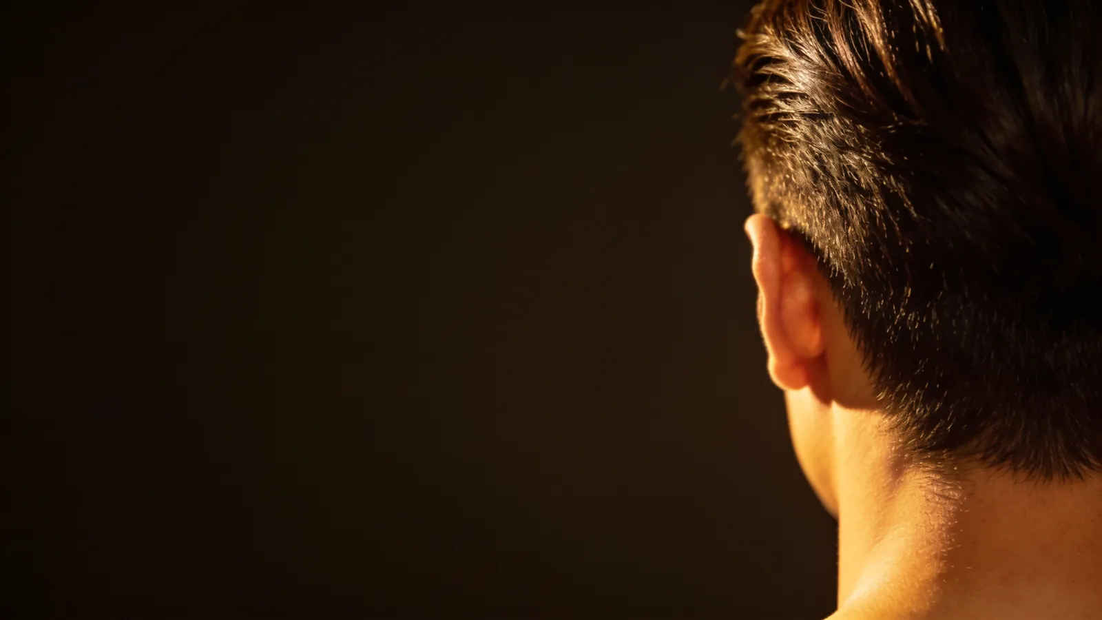 Back of a man's head with short, healthy dark hair in warm side light