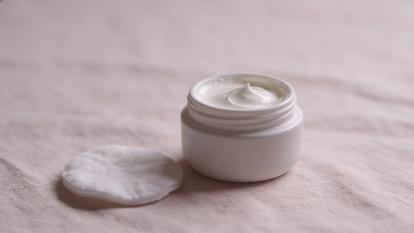 Plain cream jar and cotton pad on linen