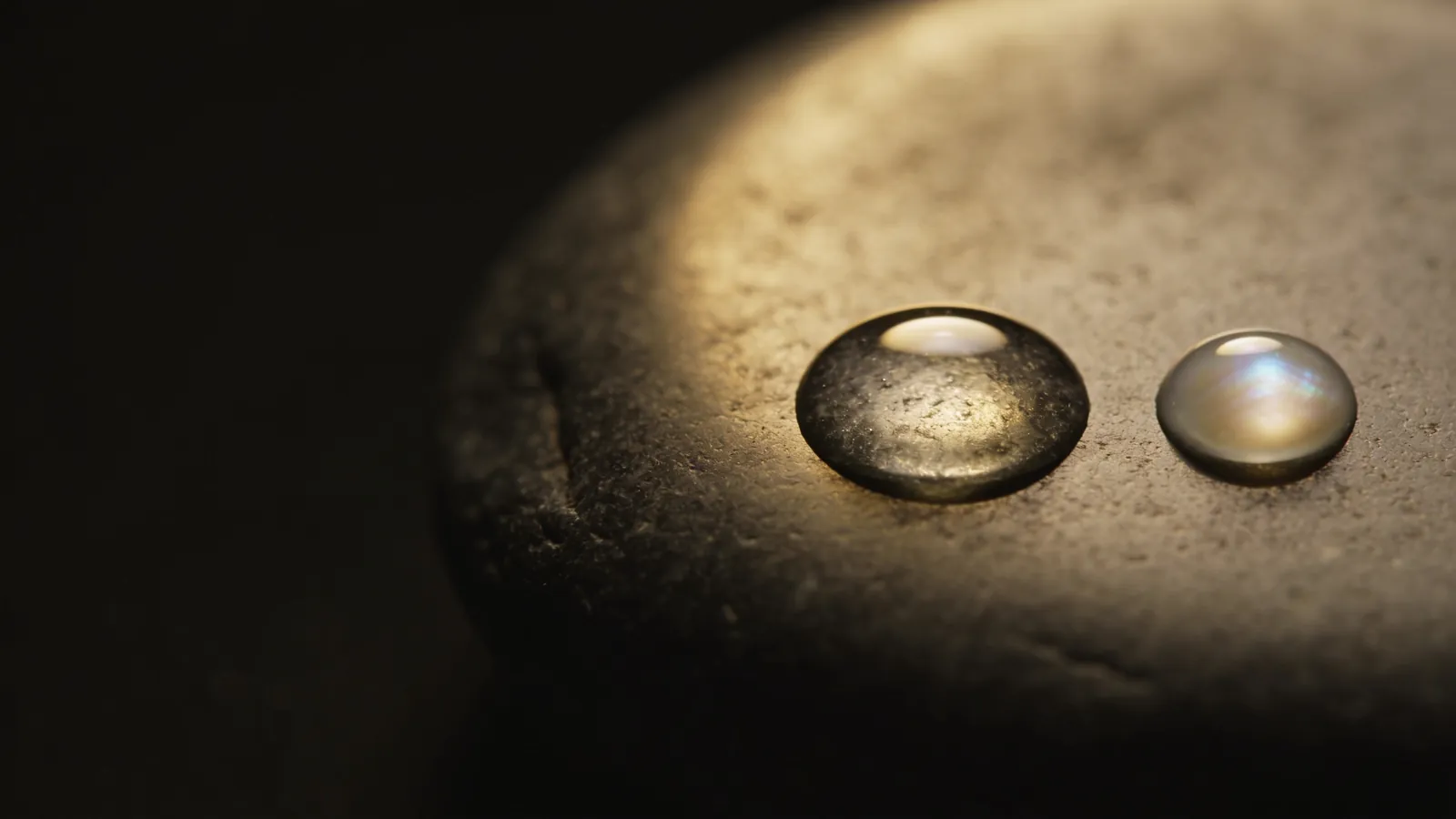 Two clear gel droplets side by side on dark stone, illustrating two skin booster types