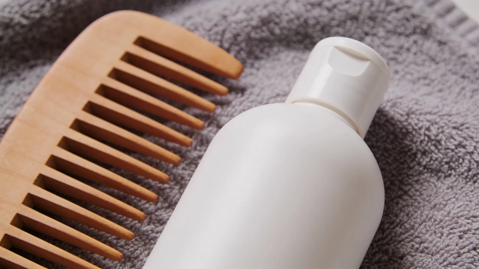 Wide-tooth comb and plain shampoo bottle on a towel