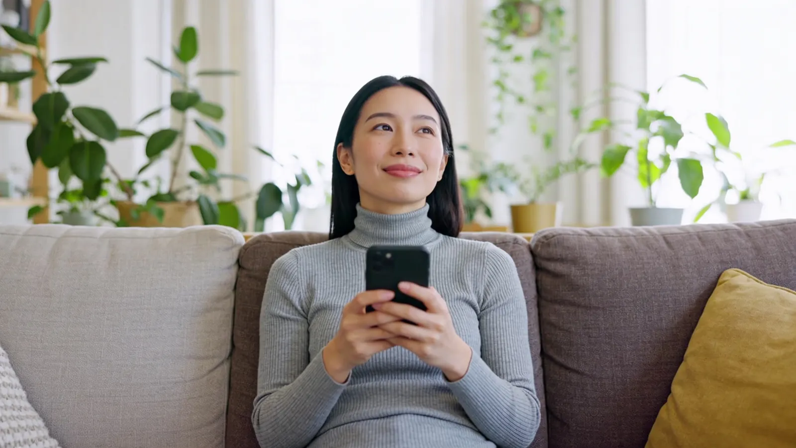 Woman sitting upright on a sofa holding her phone, illustrating neck posture
