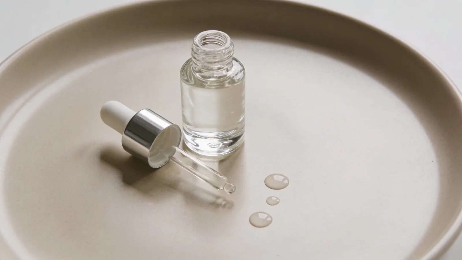 Clear serum bottle with dropper on a beige surface